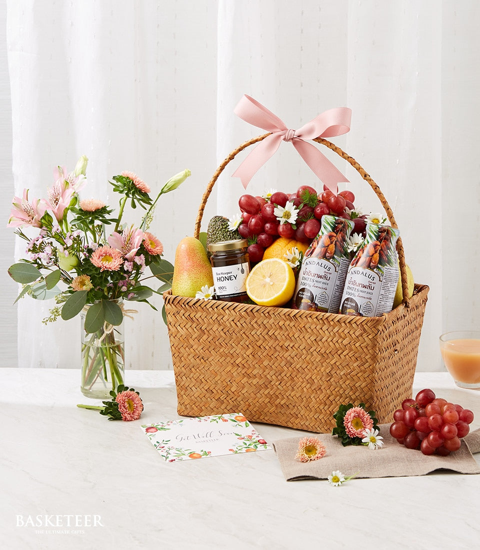 Woven fruit basket with fresh grapes, pear, honey, and dates juice paired with pink and white flowers, get well soon gift