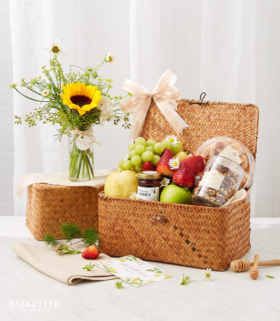 Woven straw fruit basket with fresh grapes, strawberries, pear, apple, honey and granola plus sunflower and daisy bouquet