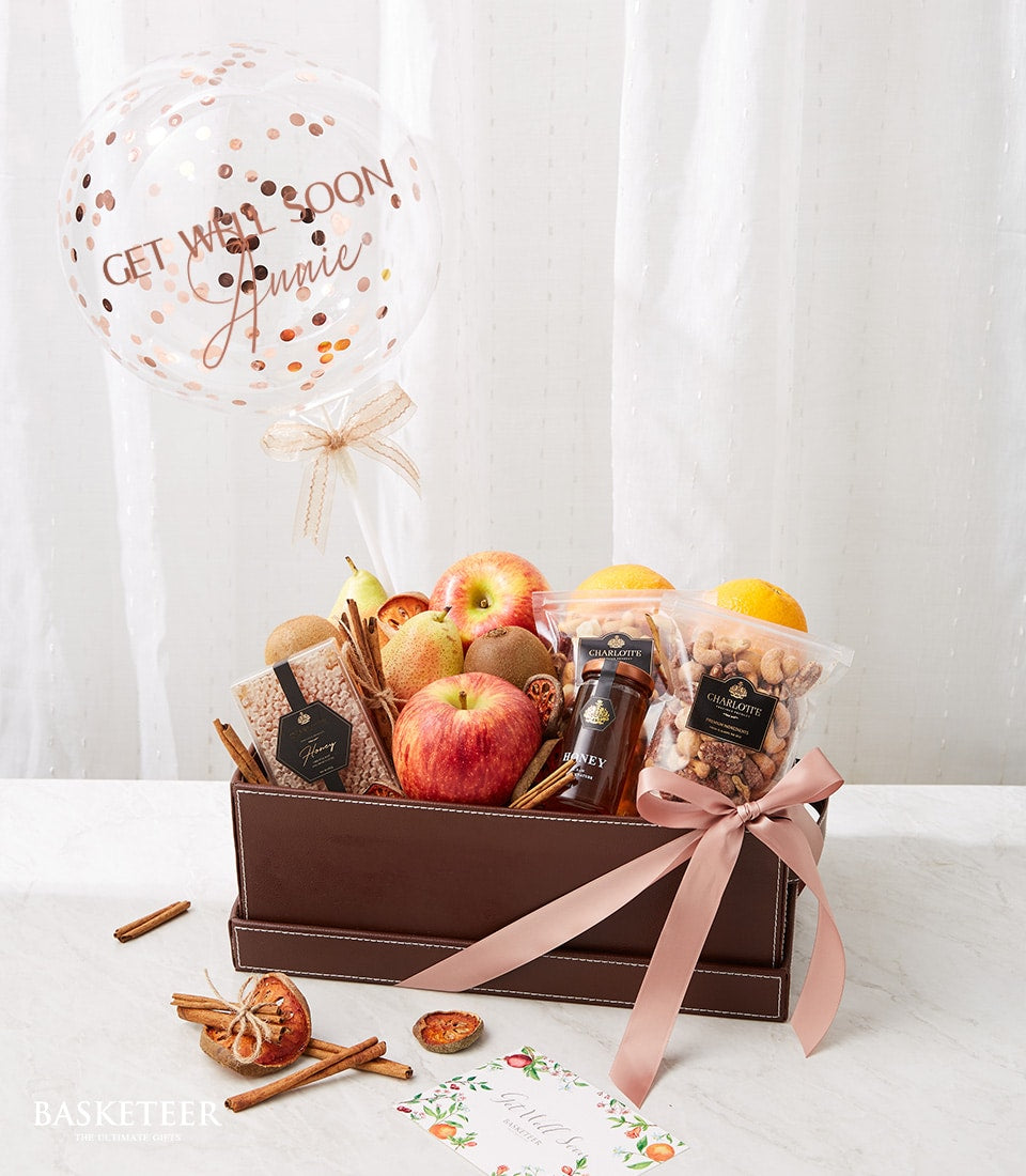 Get well soon fruit basket with apples, pears, kiwis, oranges, honey, nuts, and rose gold confetti balloon
