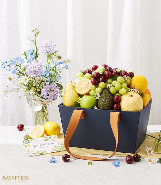 Navy fruit basket with fresh cherries, grapes, pears and mixed blooms, paired with delphinium and scabiosa arrangement for