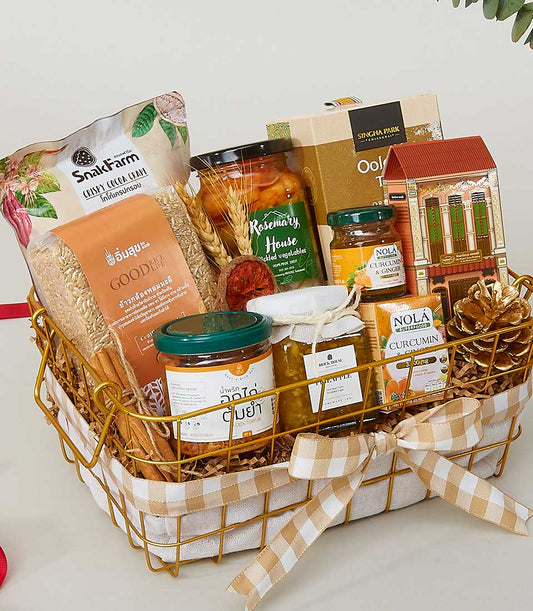 Gold wire basket with gourmet treats, jars of preserves, crispy snacks, and beige checkered ribbon for New Year gifting