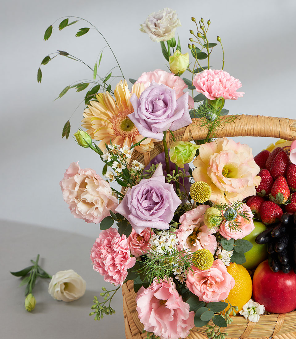 Pastel floral and fresh fruit gift basket with lavender roses, gerberas, strawberries, and grapes for birthdays