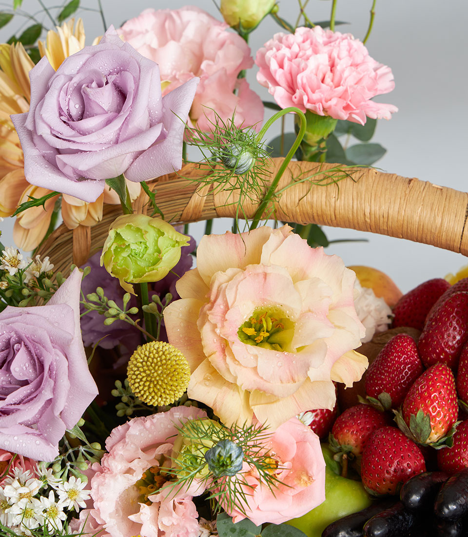 Pastel floral and fresh fruit birthday gift basket with purple roses, pink carnations, strawberries and grapes