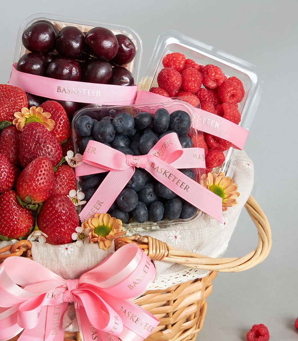 Premium wicker basket filled with fresh cherries, raspberries, blueberries, and strawberries with satin ribbon accents