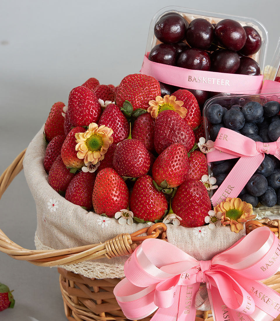 Woven wicker fruit basket with fresh strawberries, cherries, blueberries, and delicate white flowers