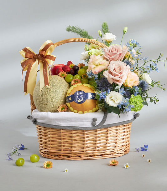 Premium wicker fruit and flower gift basket with fresh produce, pink roses, and blue lisianthus