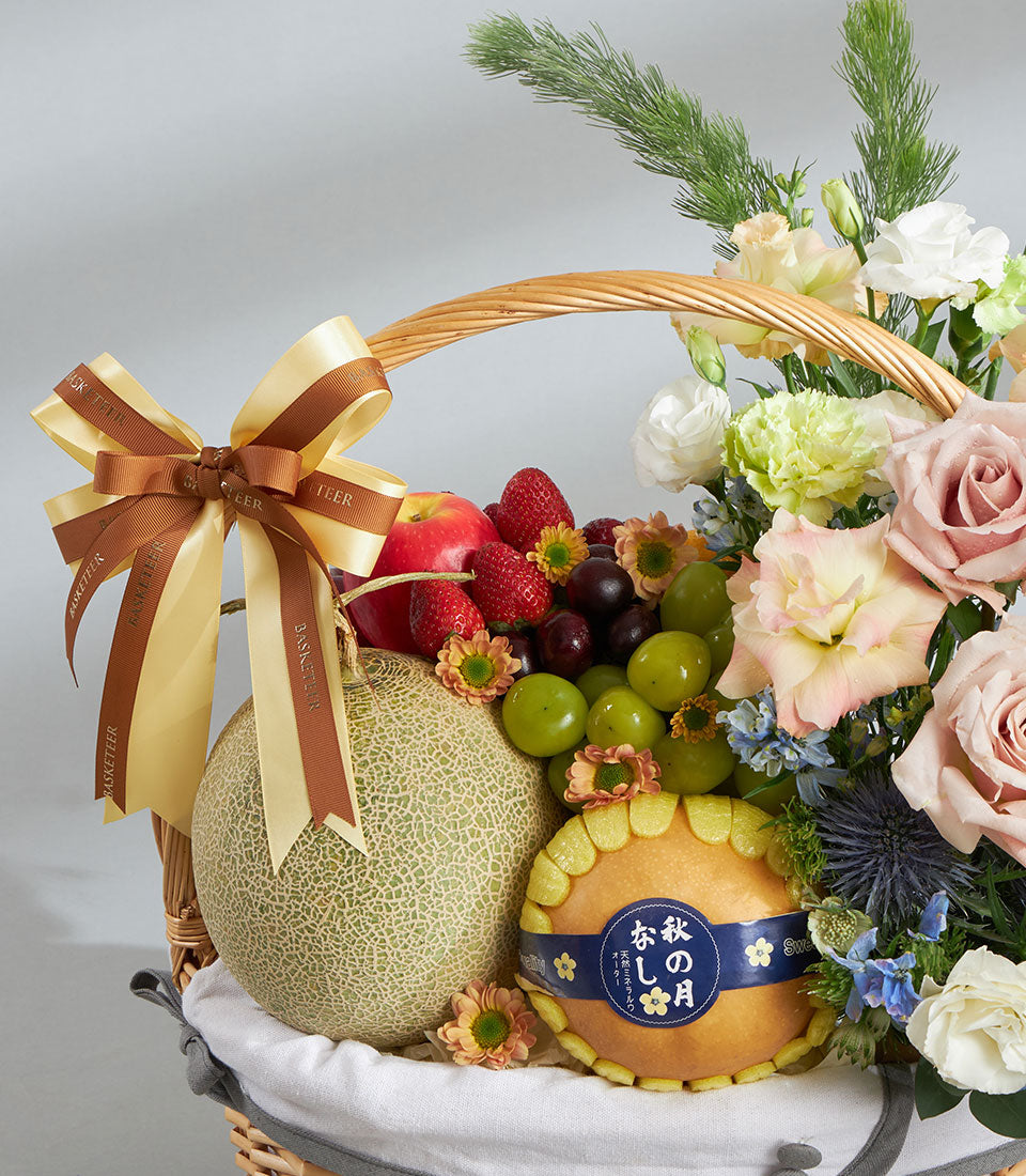 Woven wicker gift basket with fresh cantaloupe, strawberries, cherries, grapes, pear, and pastel pink roses with eustoma and