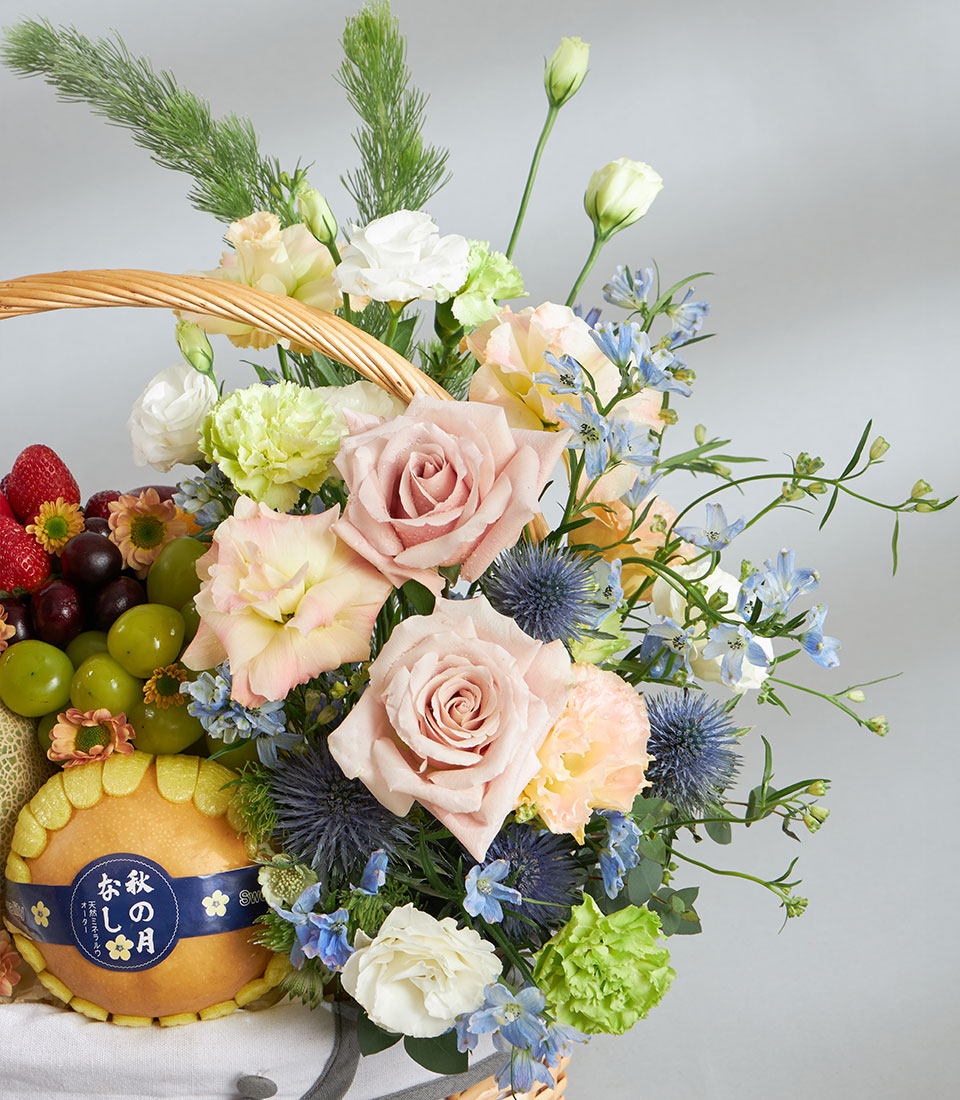 Wicker fruit and floral gift basket with fresh strawberries, cherries, grapes, pears, pale pink roses, lisianthus, and blue