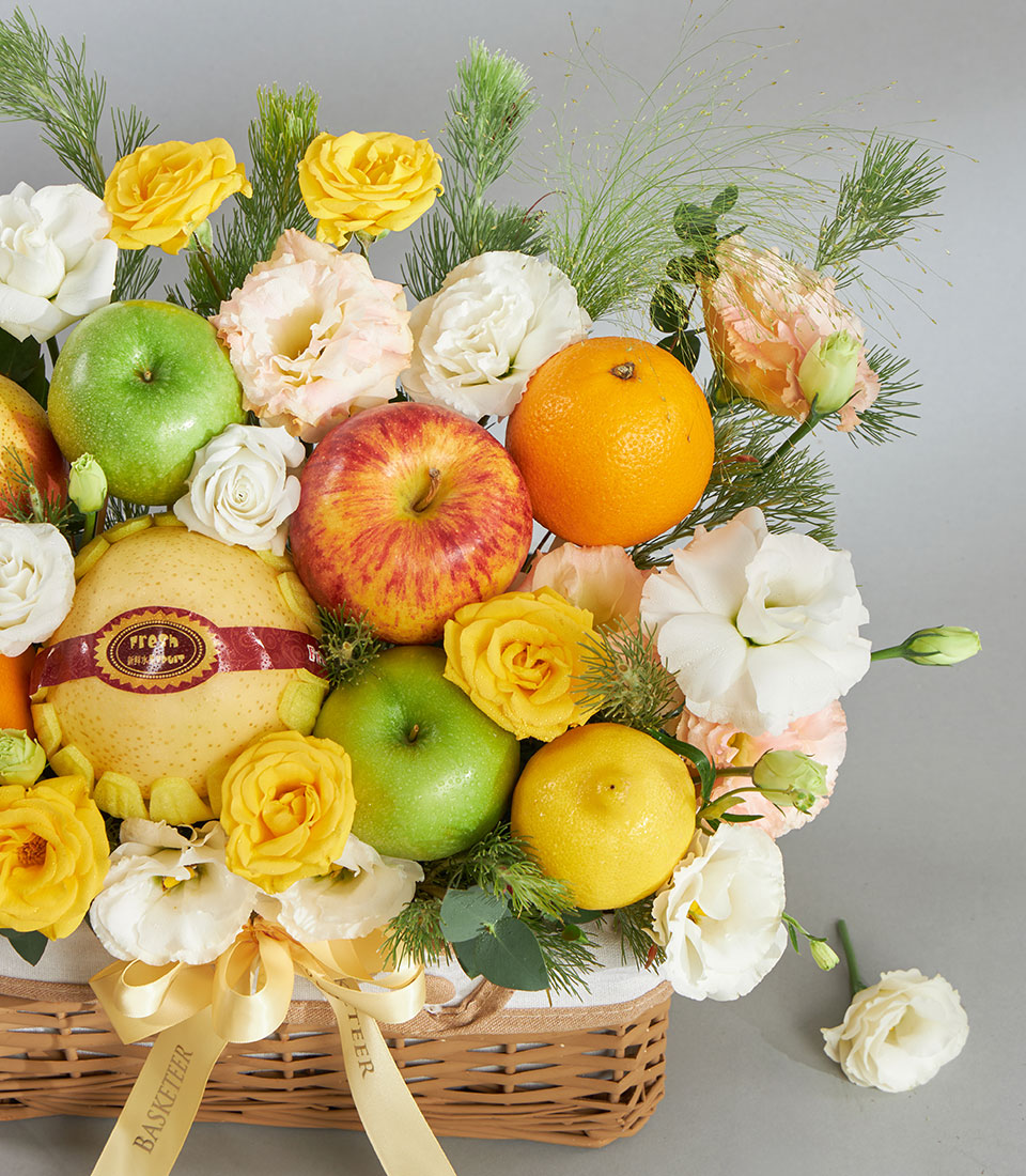 Woven wicker fruit and floral gift basket with fresh apples, pears, citrus, and cream, pink, yellow flowers