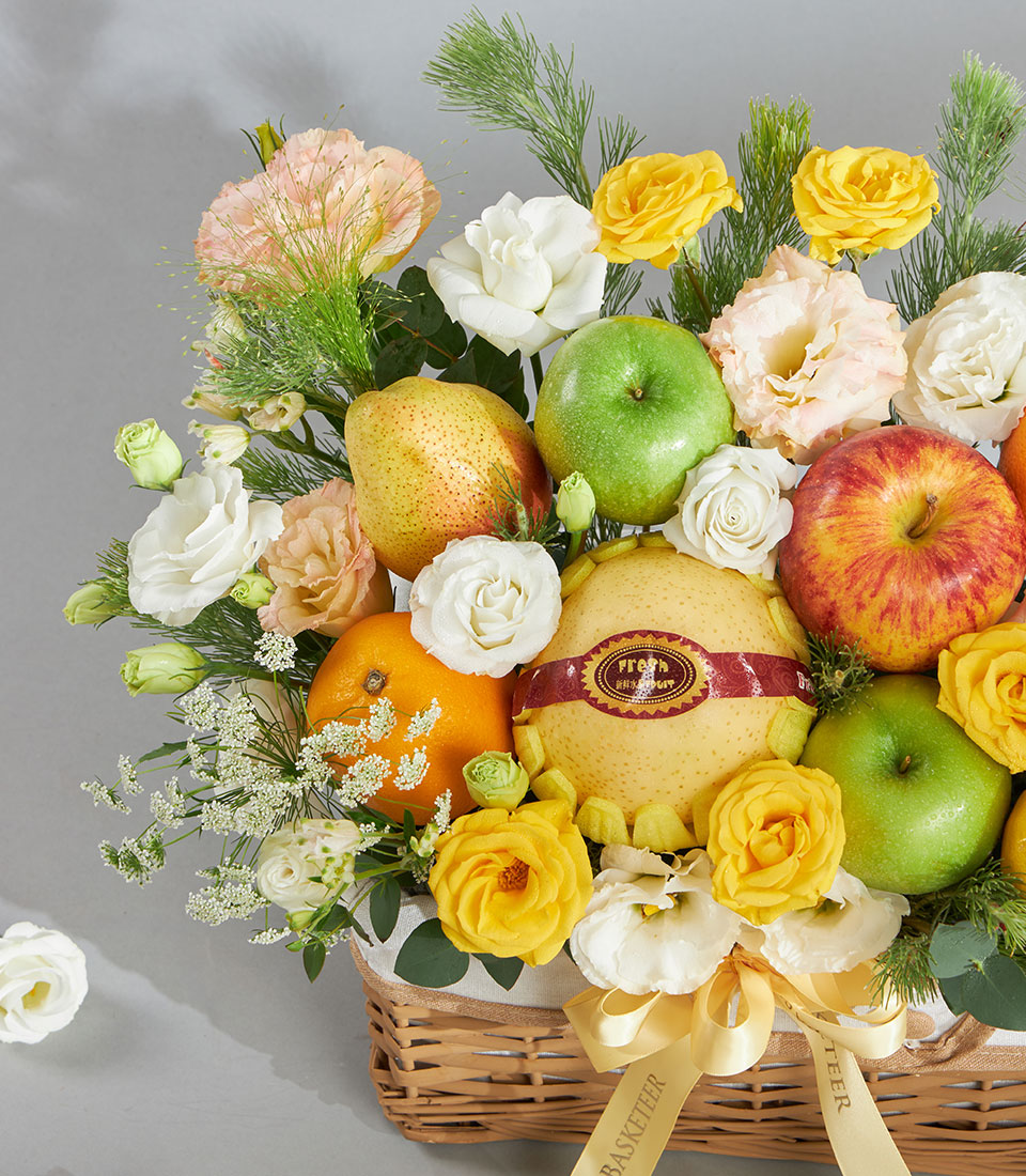 Wicker fruit and floral gift basket with fresh apples, pears, oranges, white and yellow roses, pink carnations, and green