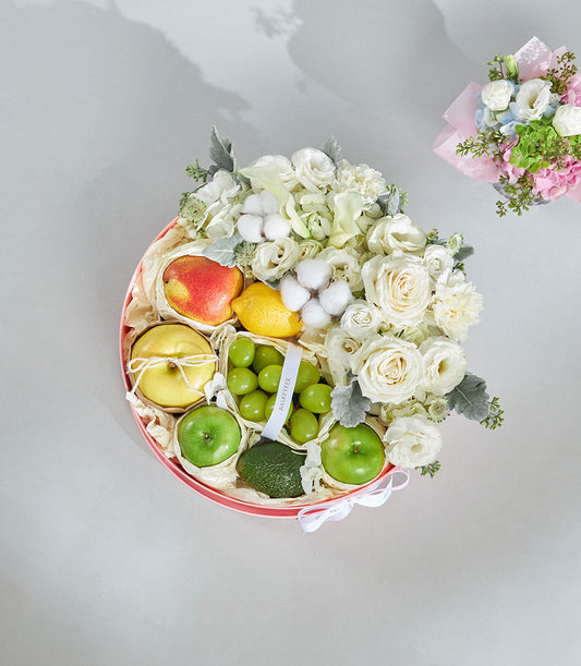 Round red gift box with fresh fruit medley and white roses, carnations, and floral accents