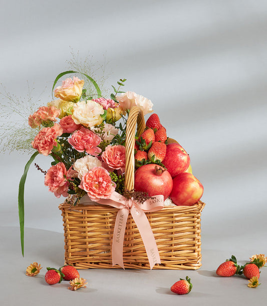 Wicker gift basket with peach carnations, strawberries, pomegranates, and apples with pink ribbon