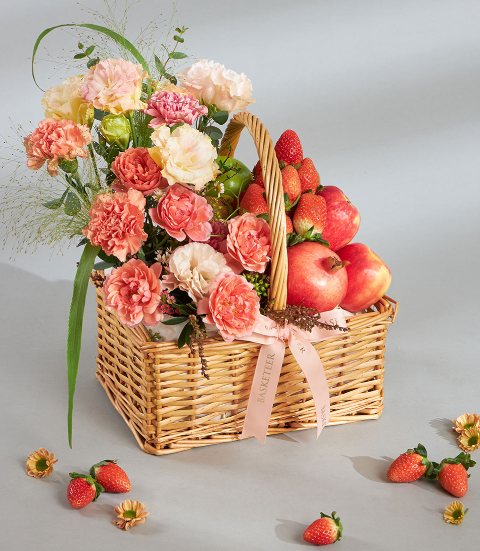 Peach pastel fruit and floral wicker gift basket with pink roses, carnations, strawberries, apples, and pomegranates