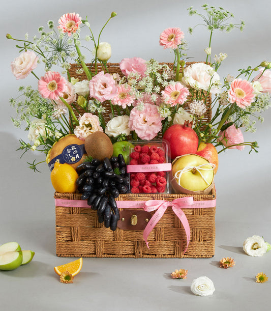 Premium fruit and pink floral gift basket with fresh produce, gerbera daisies, and carnations in woven wicker