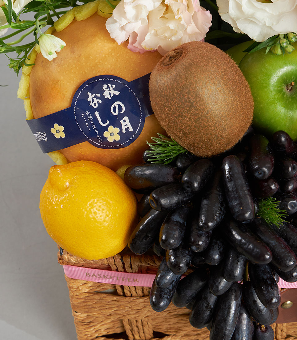 Premium fruit hamper with fresh pears, grapes, kiwi and pink florals in wicker basket