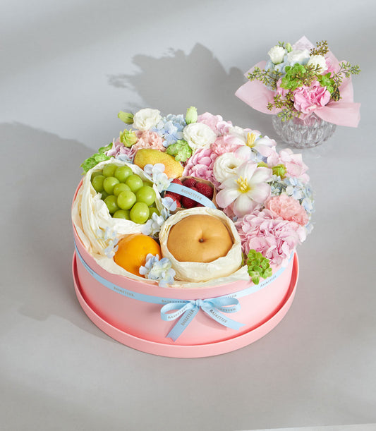 Soft pastel round gift box with fresh fruit, pink hydrangeas, and white roses for birthday celebrations