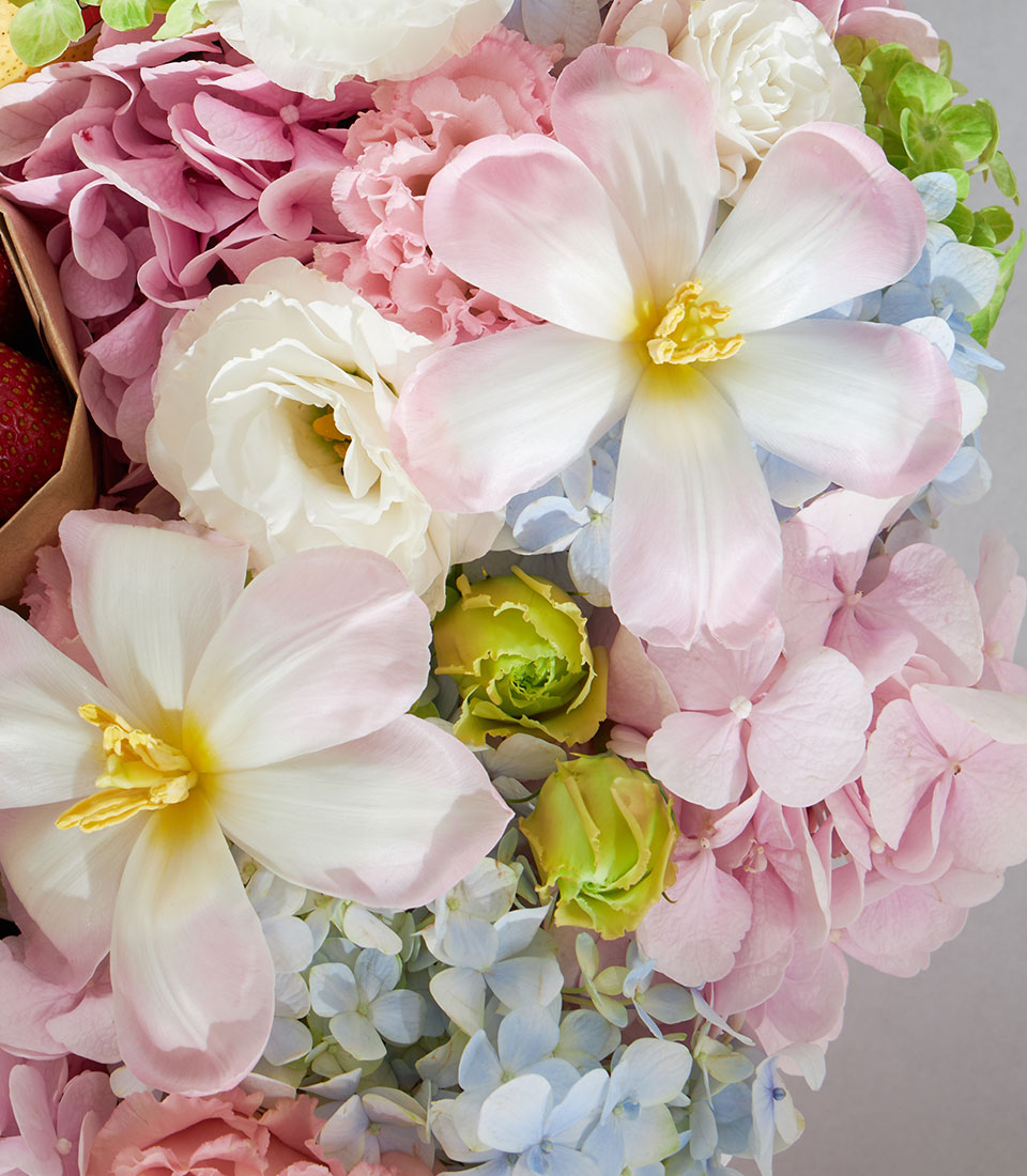 Soft pastel round gift box with white-pink tulips, hydrangeas, eustoma, and fresh strawberries for birthday celebrations