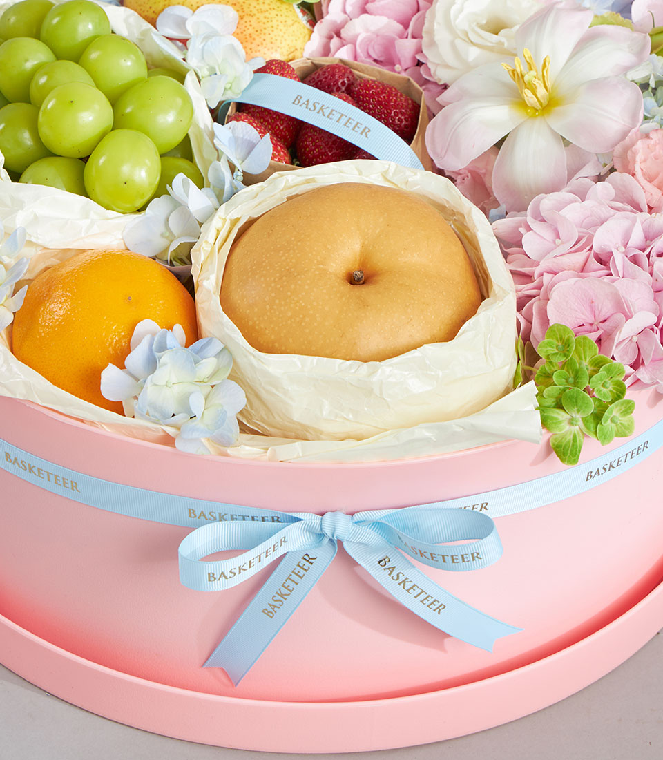Soft pastel round gift box with fresh fruits, white and pink flowers, and blue hydrangeas for birthday