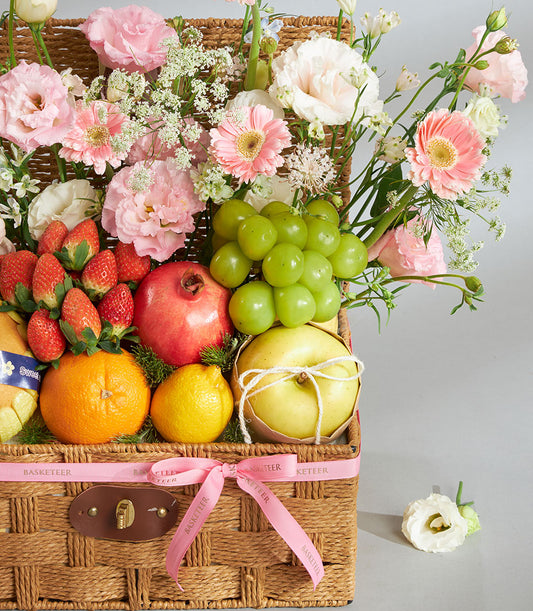 Premium pink pastel fruit and floral gift basket with fresh strawberries, pomegranate, grapes, citrus, and ruffled blooms in