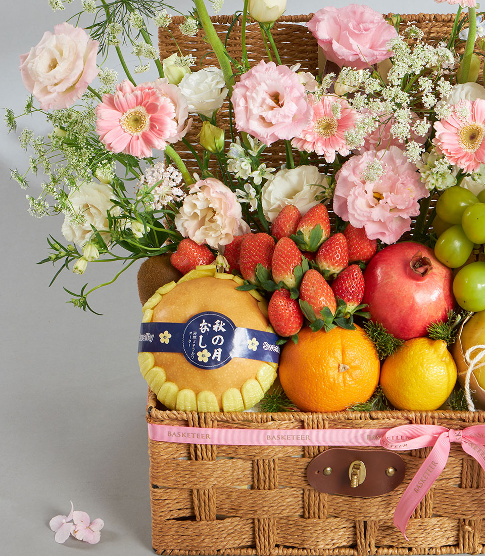 Pink pastel fruit and floral gift basket with roses, strawberries, pear, and pomegranate in woven wicker