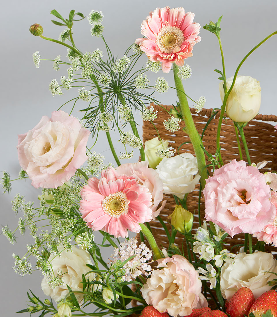 Pink Gerbera daisies, Eustoma roses, and fresh strawberries in woven basket gift arrangement