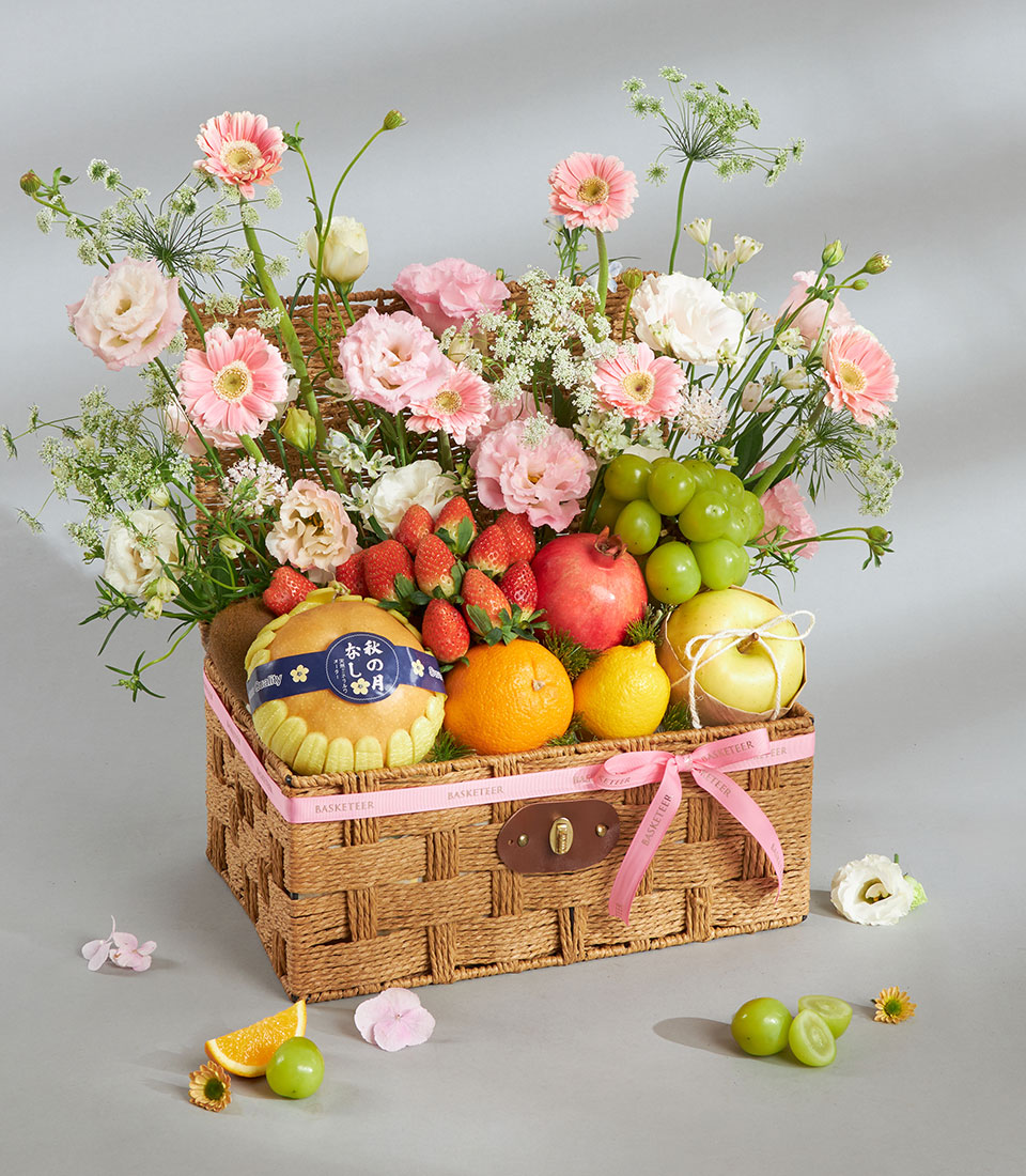 Pink pastel fruit and floral gift basket with fresh berries, citrus, and gerbera daisies in woven wicker