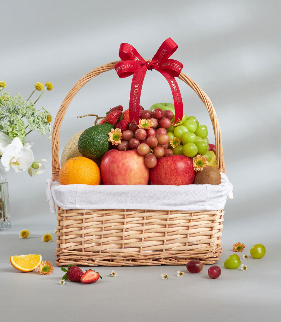 Woven wicker fruit basket with red ribbon bow filled with imported apples, grapes, orange, kiwi and cantaloupe