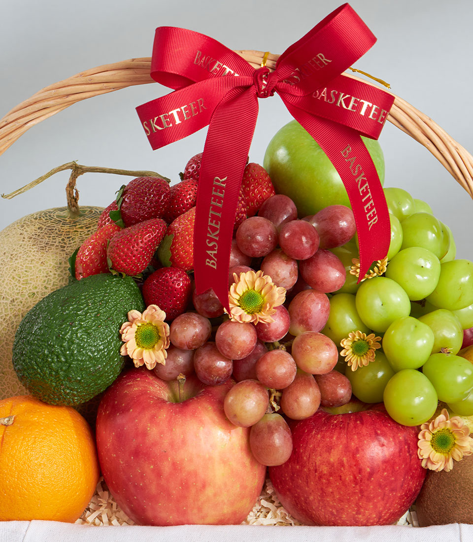 Woven wicker fruit basket with fresh cantaloupe, apples, grapes, strawberries and avocado, tied with red ribbon