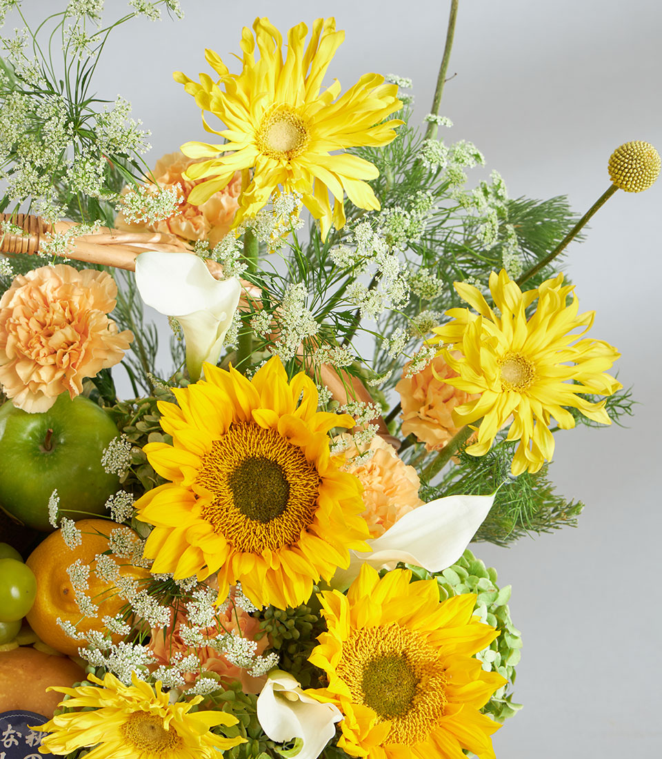 Bright yellow and orange floral basket with sunflowers, gerberas, fresh fruit and white calla lilies
