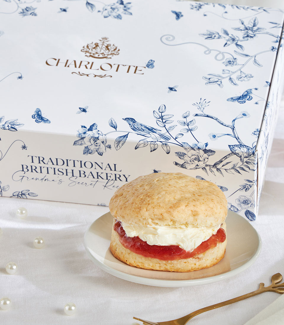 Golden-brown British scone with jam and cream on decorative Charlotte Bakery box, elegant gift presentation