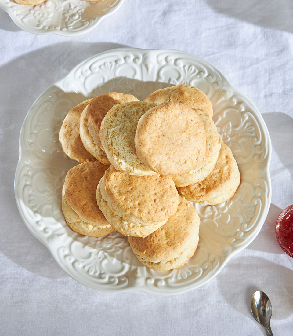 Golden-brown British scones with jam on ornate ceramic platter, artisan bakery gift set