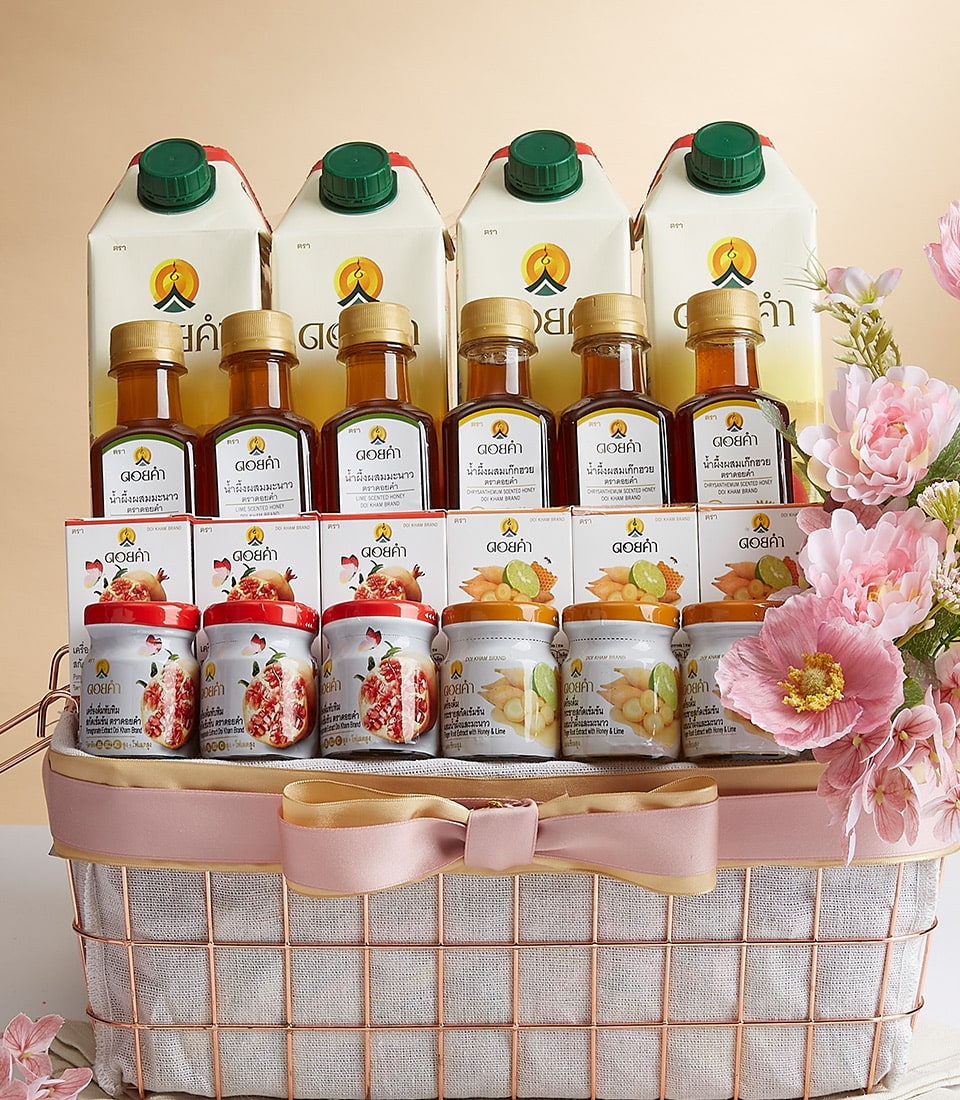 Rose gold wire mesh gift basket with white lining, pink bow, four beverage cartons, golden honey bottles, and pomegranate,