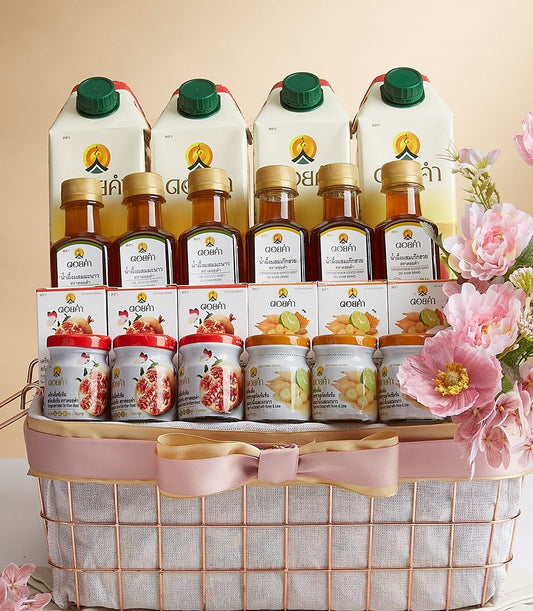 Rose gold wire mesh gift basket with white lining, pink bow, four beverage cartons, golden honey bottles, and pomegranate,