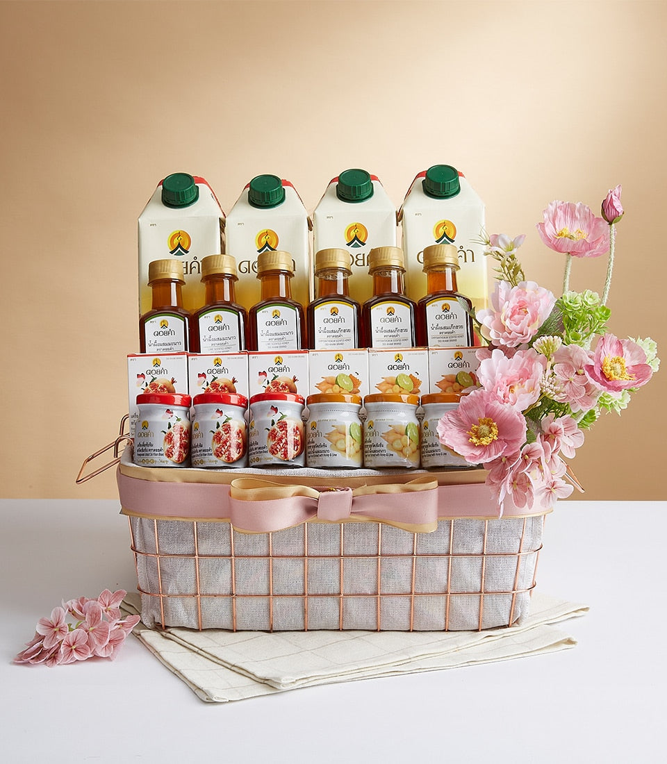 Rose gold wire mesh gift basket with pink ribbon, filled with premium wellness products and fresh pink and white flowers