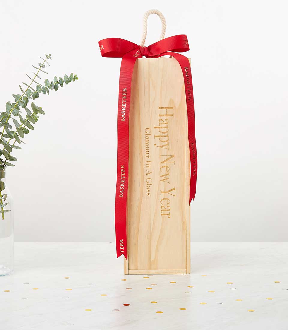 Premium red wine gift in engraved pine box with red ribbon and New Year greeting, styled with eucalyptus and gold confetti