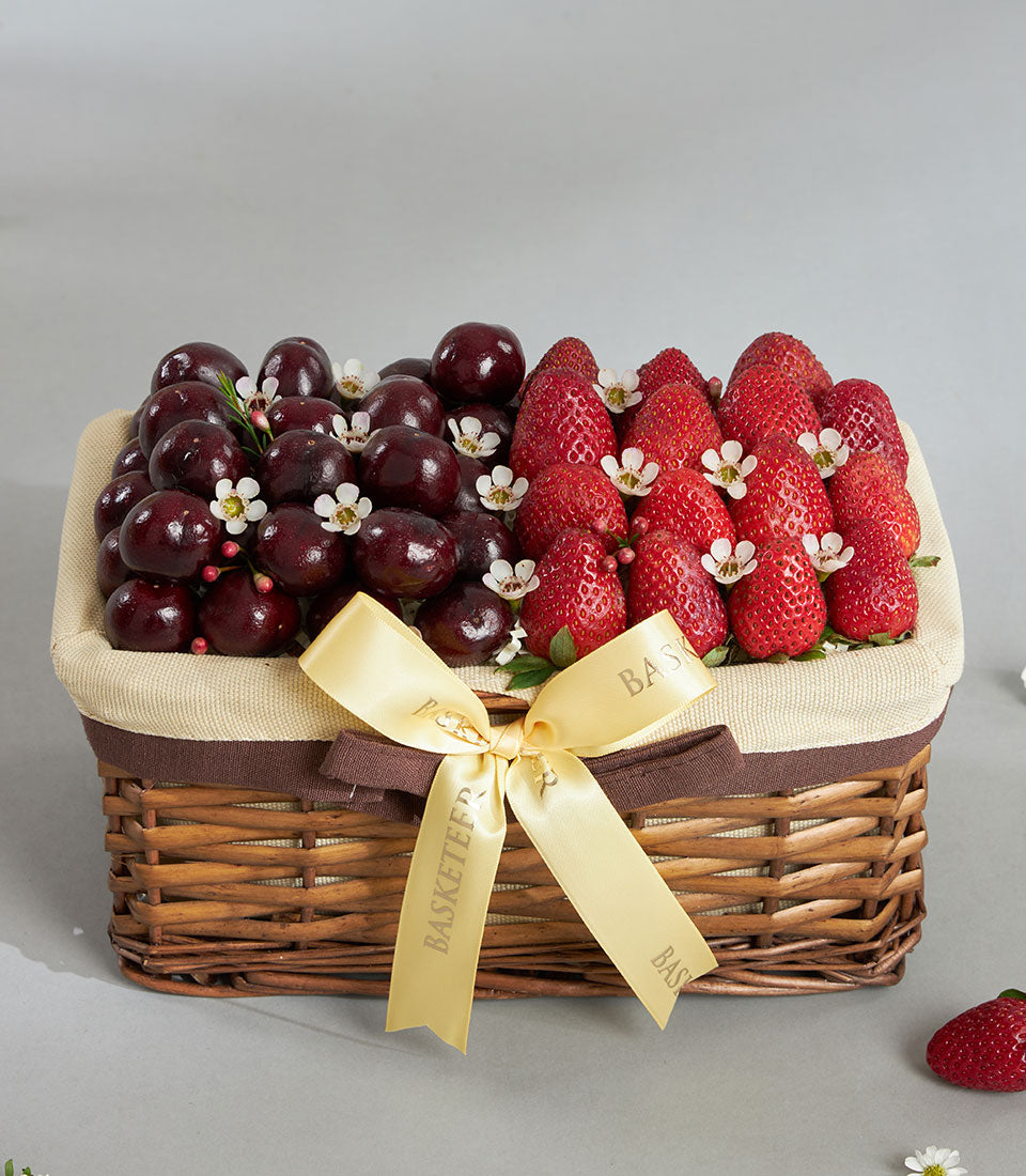 Premium cherry and strawberry gift basket with golden ribbon and white blossoms in woven wicker