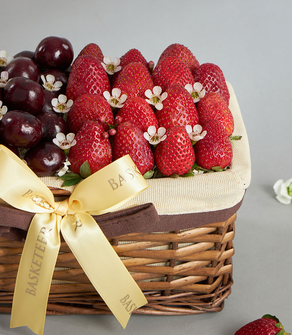 Woven wicker basket filled with fresh dark red cherries and bright strawberries, tied with brown and yellow ribbon bow