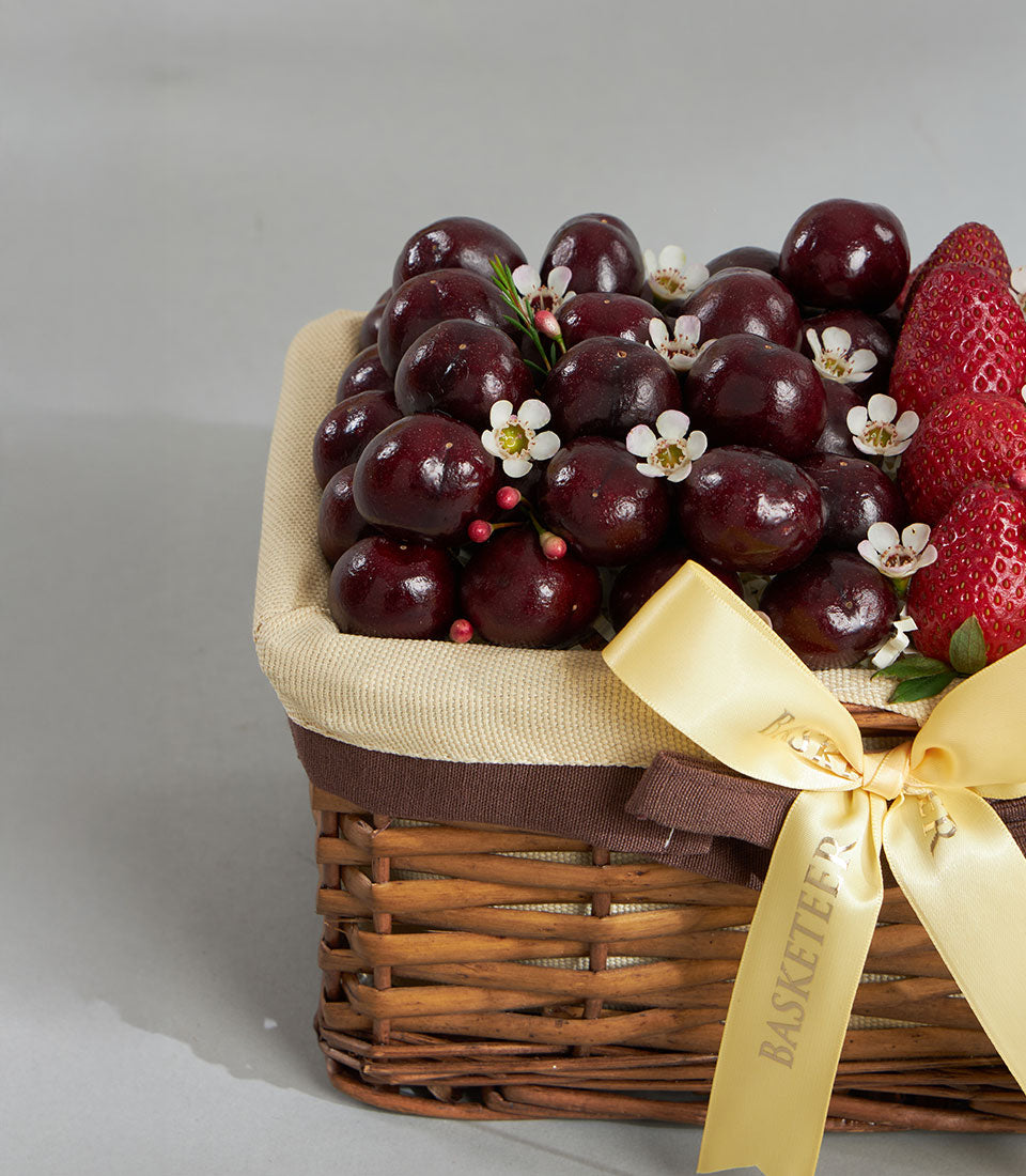 Luxury cherry and strawberry gift basket with white flowers, woven wicker base, and satin ribbon bow
