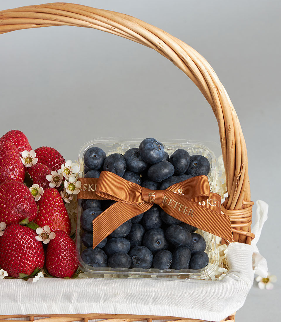 Rustic wicker basket with fresh red strawberries and blueberries in clear container, white tissue, artisan fruit gift