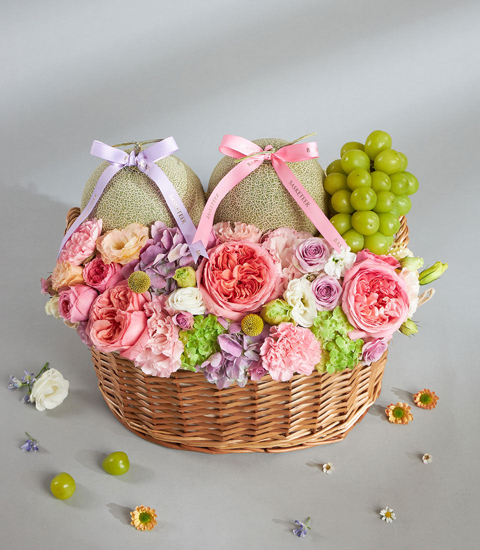 Pastel melon and rose gift basket with lavender and pink ribbon, fresh grapes, and mixed flowers