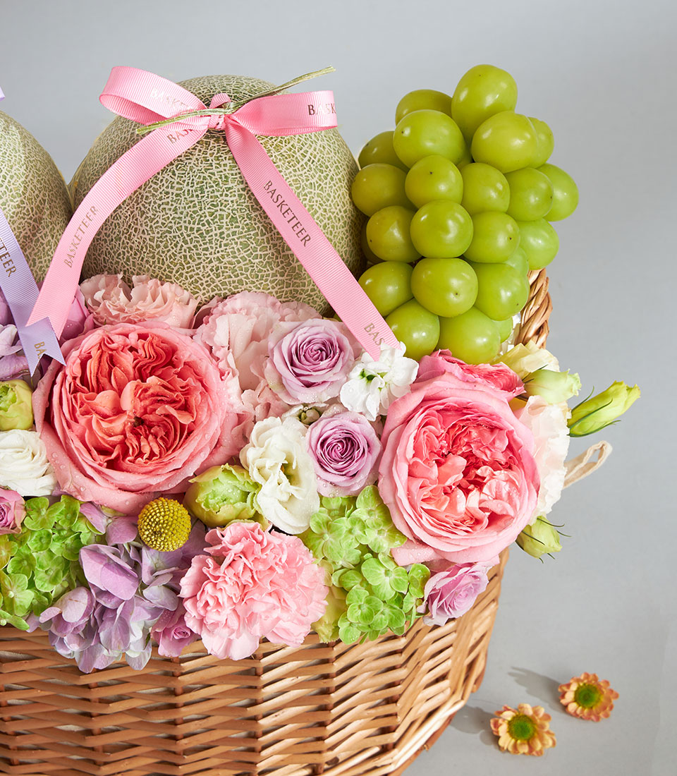 Pastel melon and garden rose gift basket with green grapes and hydrangeas in woven wicker