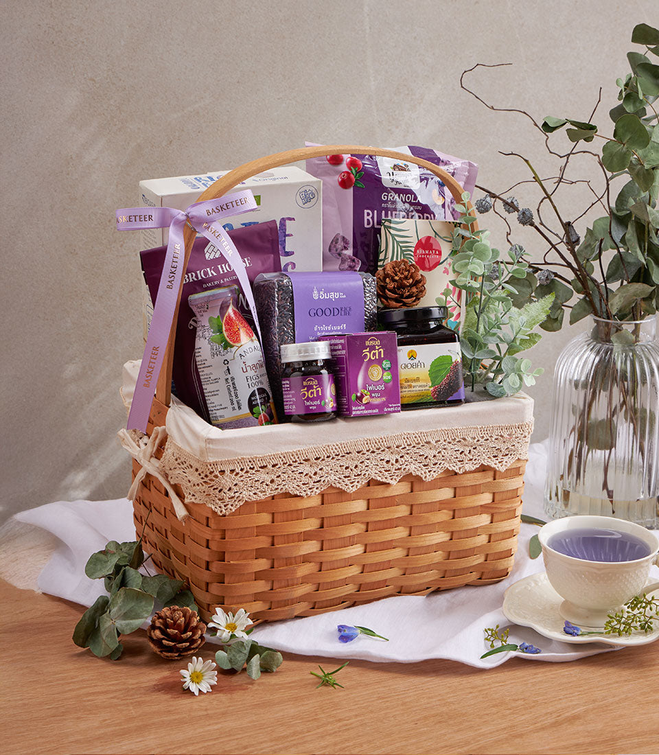 Purple wellness gift basket with blueberry granola, superfood rice, fig juice, and health supplements in woven wood hamper