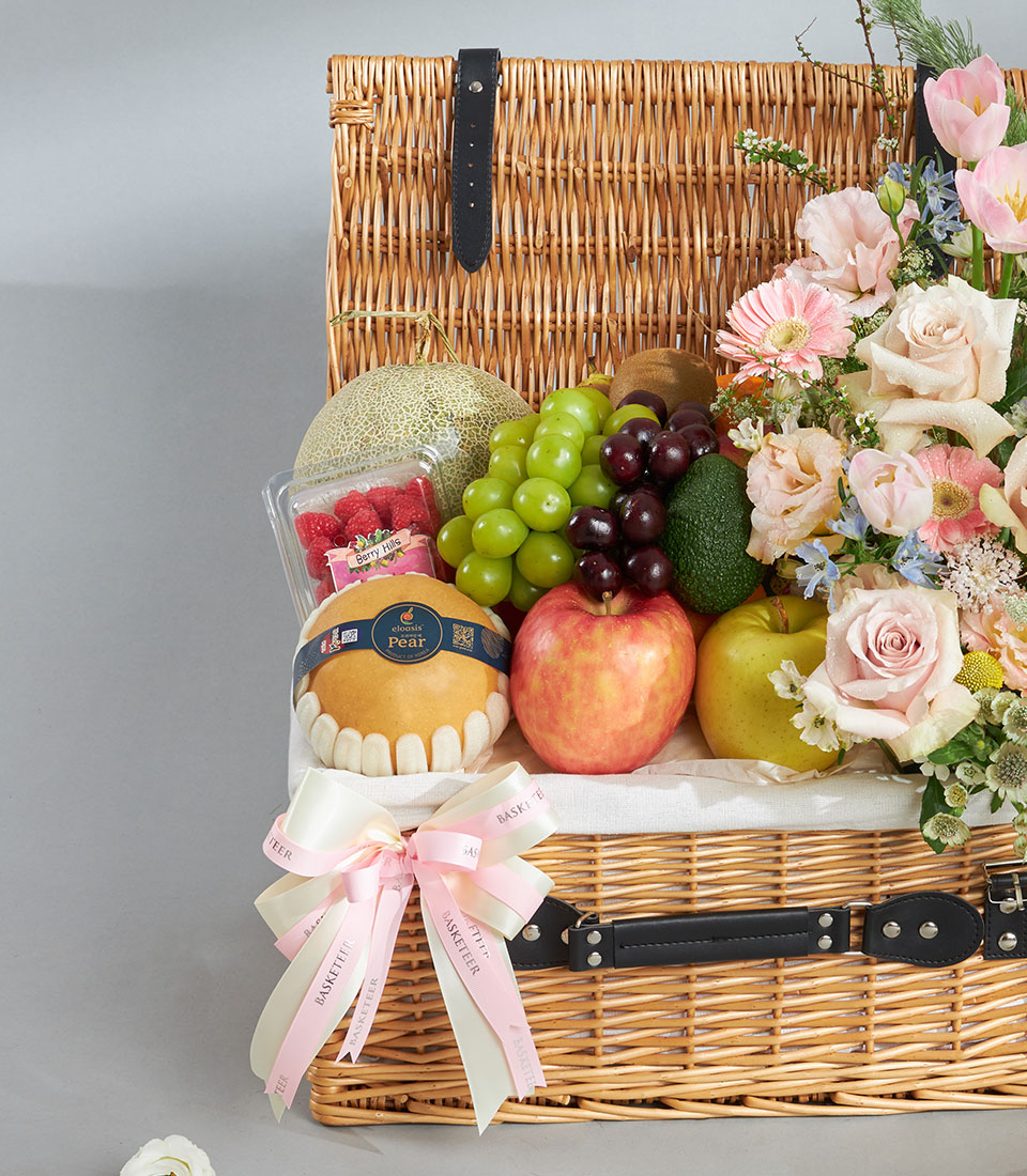 Luxury wicker basket with fresh Shine Muscat grapes, tropical fruits, and pink rose bouquet arrangement