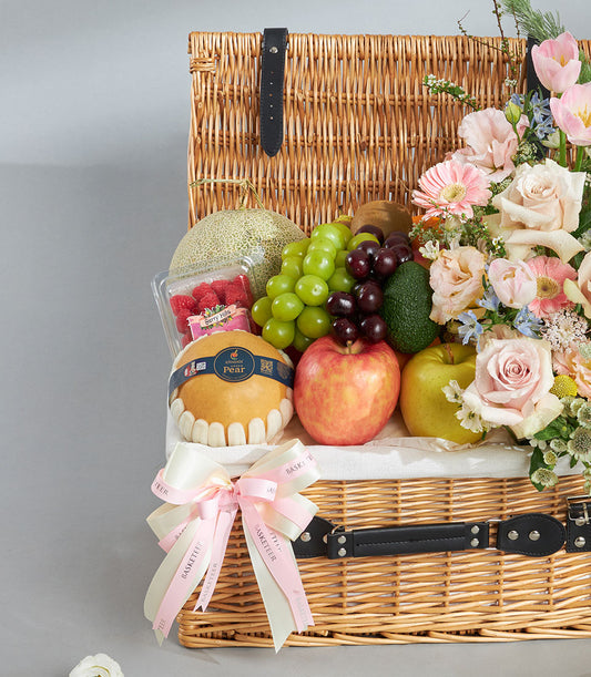 Luxury wicker basket with fresh Shine Muscat grapes, tropical fruits, and pink rose bouquet arrangement
