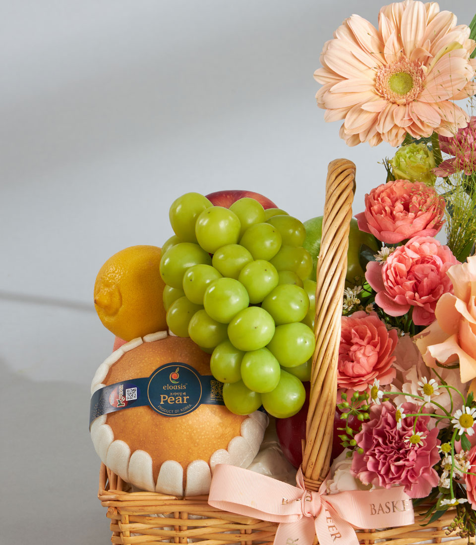 Woven wicker fruit basket with fresh peach gerberas, apples, grapes and pears, tied with pink ribbon for birthday gifting
