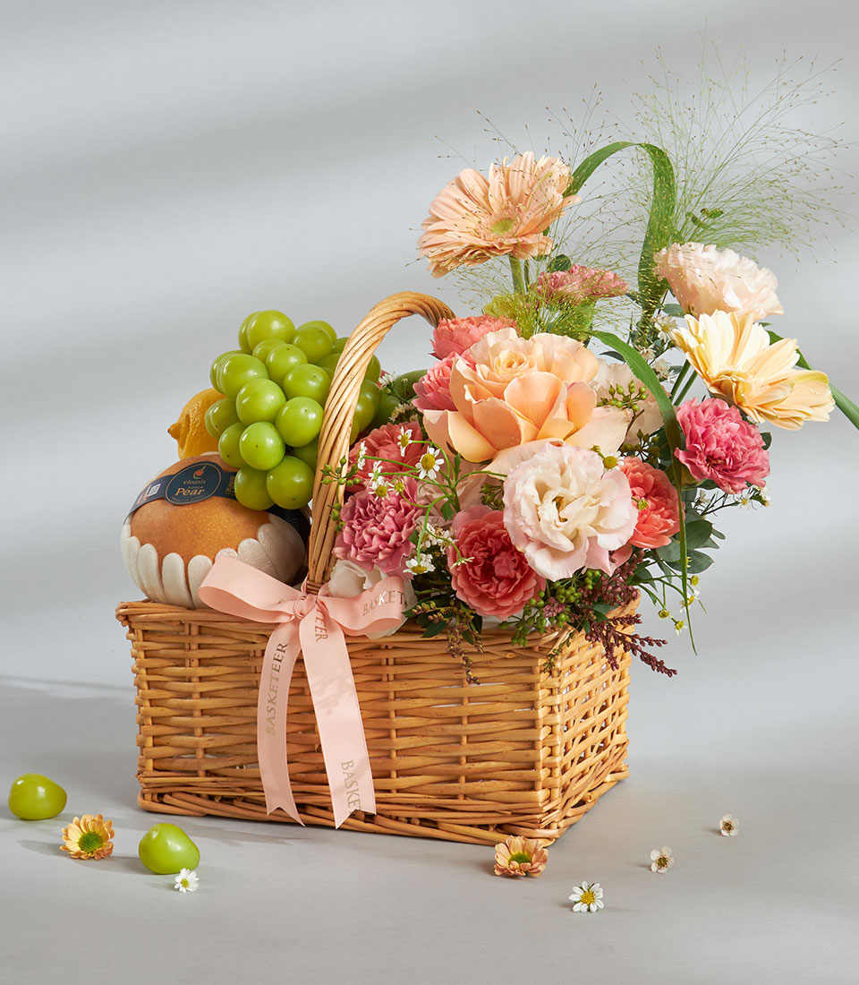 Soft peach and pink floral arrangement with fresh fruit in woven wicker basket for birthday gifting