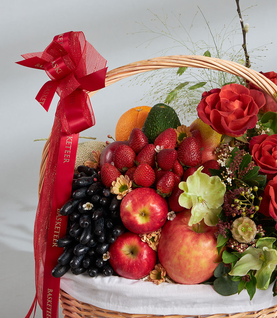 Basketeer premium hamper delivery Thailand: wicker basket overflowing with ripe strawberries, apples, grapes and vibrant red roses. Tied with a red Basketeer ribbon.