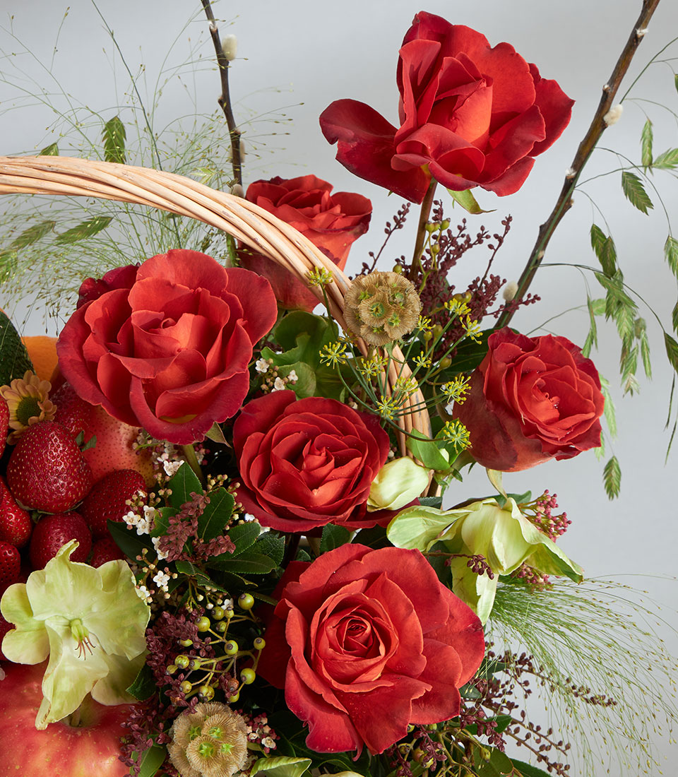 Lush Basketeer fruit gift basket overflowing with red roses, fresh strawberries and apples, artfully arranged in a wicker hamper.