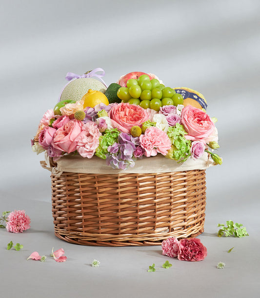 Woven wicker basket overflowing with fresh fruits, pink roses, and purple hydrangeas in pastel arrangement