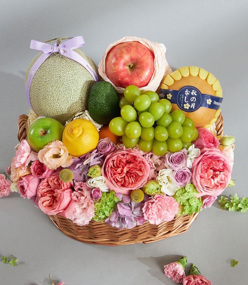 Woven wicker basket with fresh tropical fruits and pastel pink, coral, and purple roses, carnations, and hydrangeas